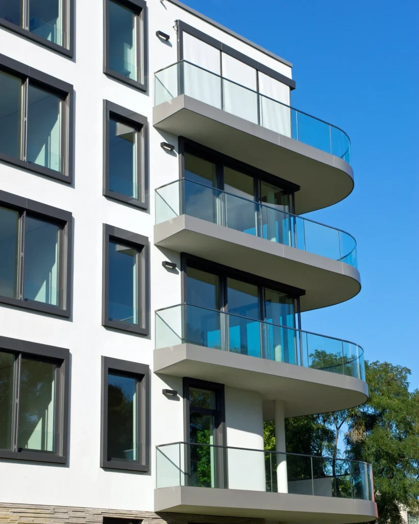 Contemporary apartment building with glass balconies and large windows on a sunny day.
