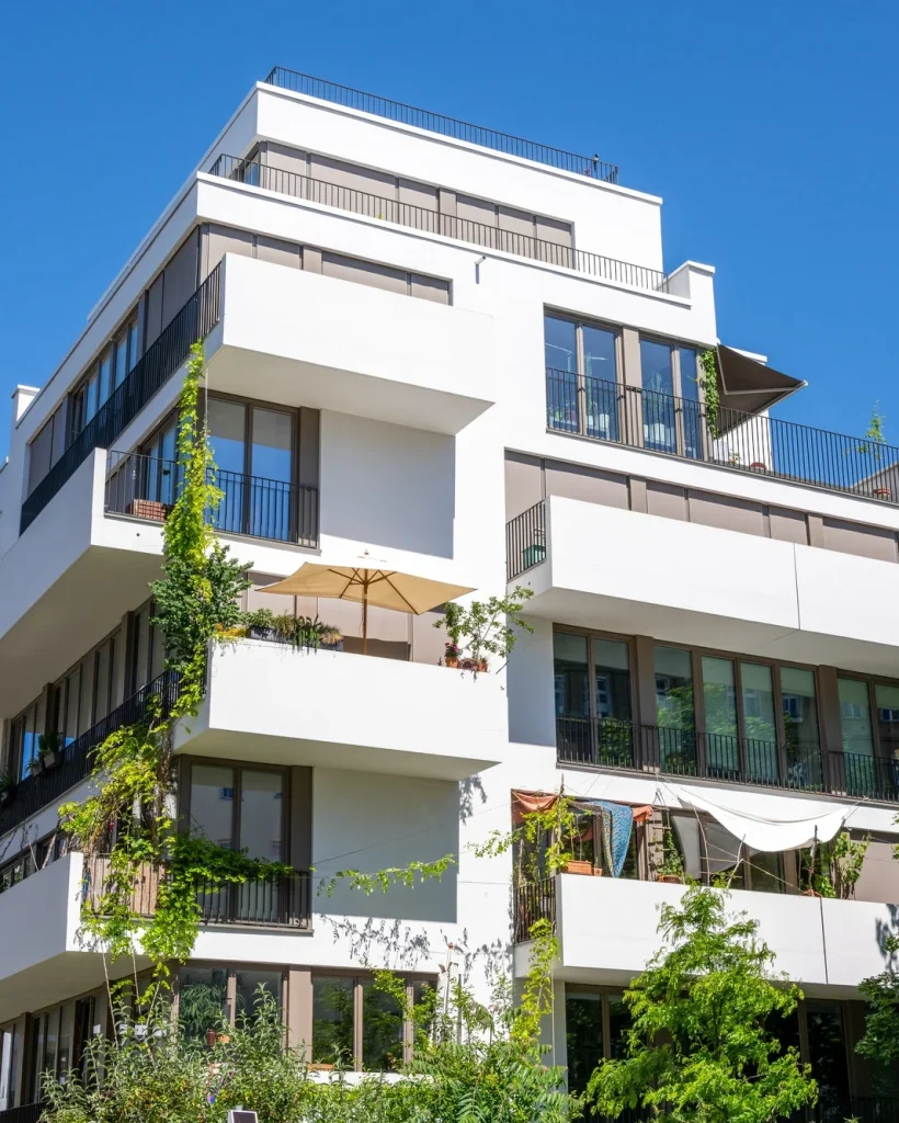 Contemporary white apartment building with green balconies and clear blue sky.